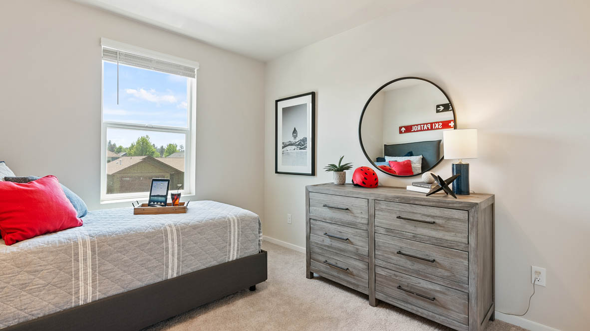 Monrovia bedroom with a bed and red accent pillow, a dresser with a rounded mirror and lamp, and window