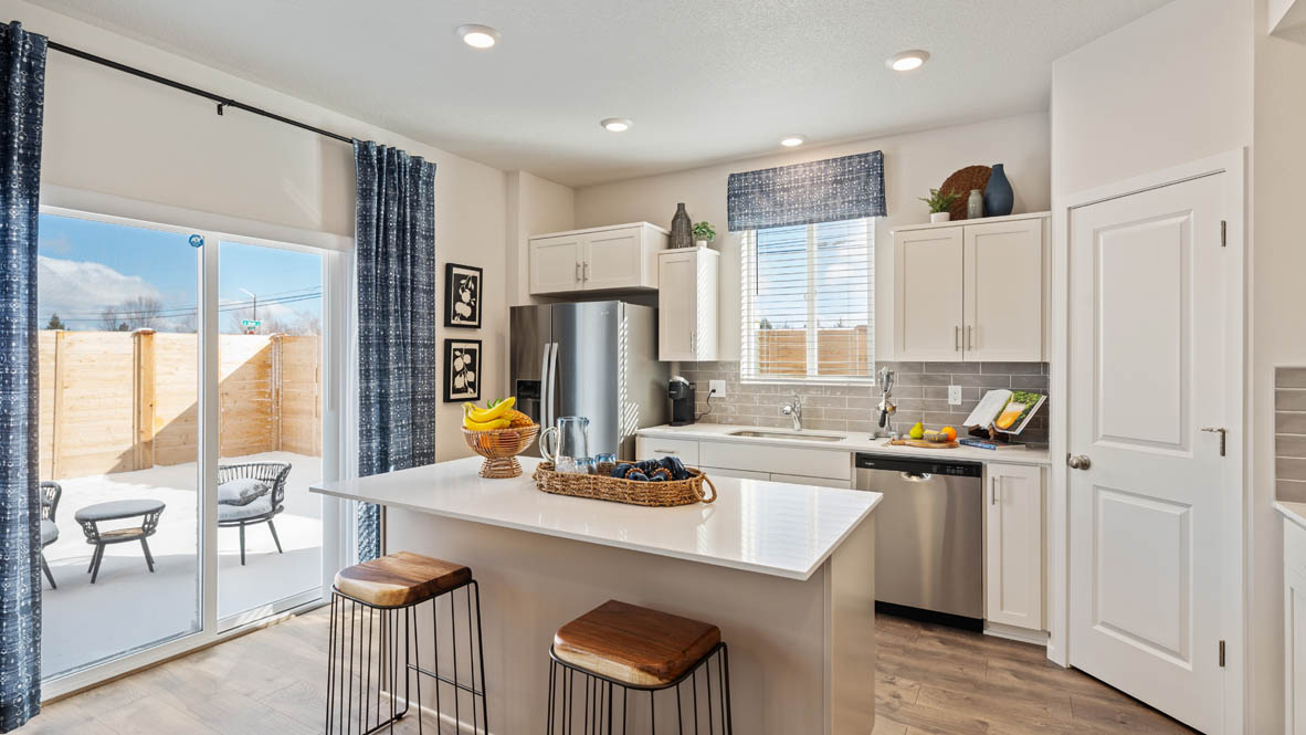 Monrovia Kitchen with island that has white quartz countertops, two seats set up at the island, stainless steel appliances, a sliding glass door to the backyard, and white shaker style cabinets