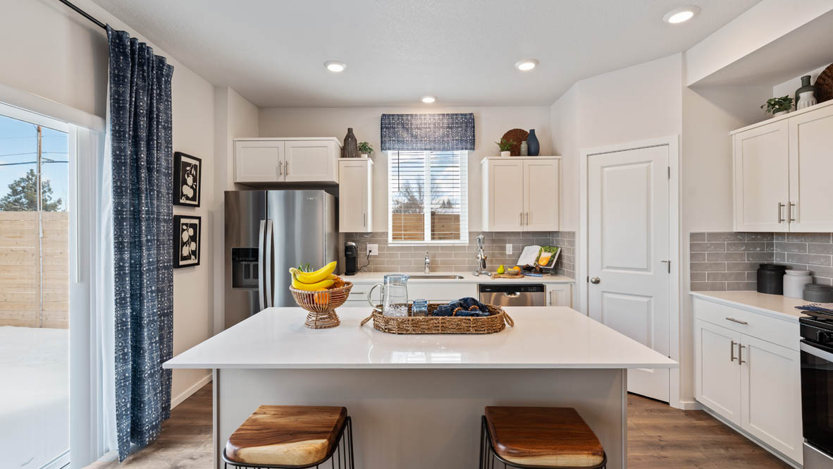 Monrovia Kitchen with island that has white quartz countertops, two seats set up at the island, stainless steel appliances, a sliding glass door to the backyard, and white shaker style cabinets