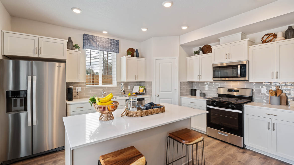 Monrovia Kitchen with island that has white quartz countertops, two seats set up at the island, stainless steel appliances, a sliding glass door to the backyard, and white shaker style cabinets