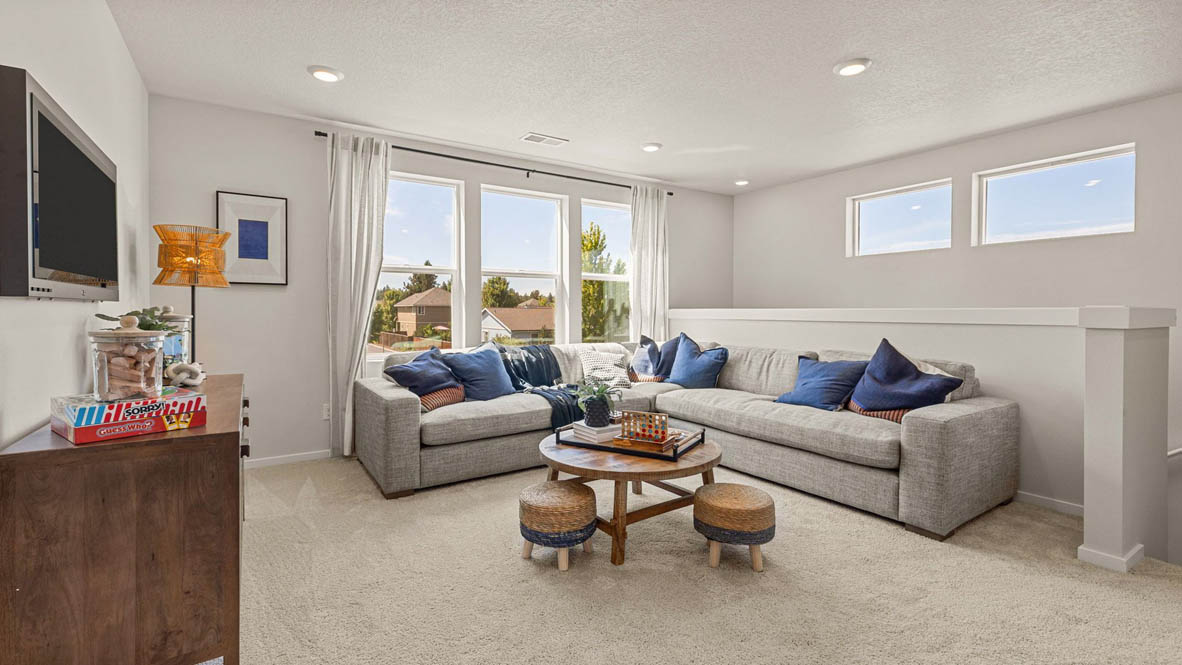 Monrovia carpeted Loft space with L shaped sectional couch, circular wooden coffee table with two small stools, a TV with a medial console underneath and three windows with drapes