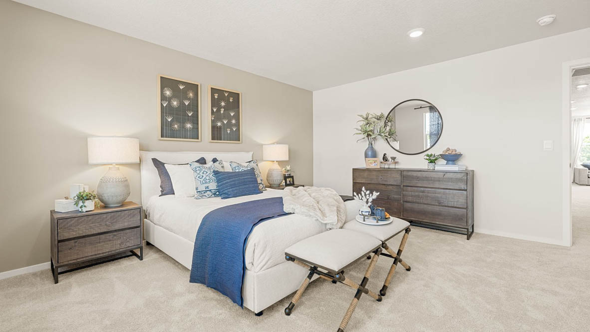 Monrovia Primary bedroom with light gray accent wall, large bed with seating bench at the end, light gray wooden furniture, and blue bedding accents