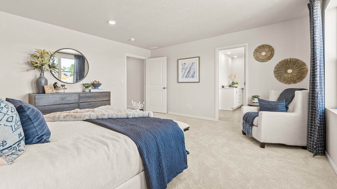 Monrovia Primary bedroom with light gray accent wall, large bed with seating bench at the end, light gray wooden furniture, and blue bedding accents with a chair in the corner