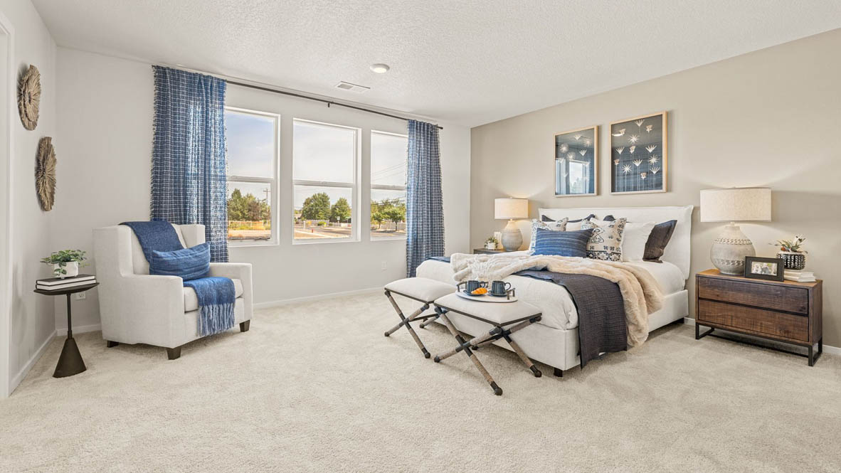 Monrovia Primary bedroom with light gray accent wall, large bed with seating bench at the end, light gray wooden furniture, and blue bedding accents with a chair in the corner