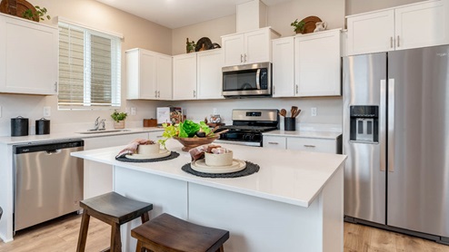 Lowrie Estates kitchen with white quartz countertops, stainless steel appliances, a kitchen island, and white shaker style cabinets