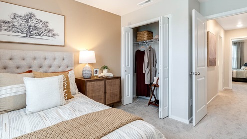 Lowrie Estates bedroom with light beige accent wall, white bedding, orange window drapes, and wooden accent table
