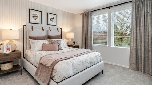 Lowrie Estates Primary bedroom with king bed and carpeting flooring with two accent tables and drapes on the windows