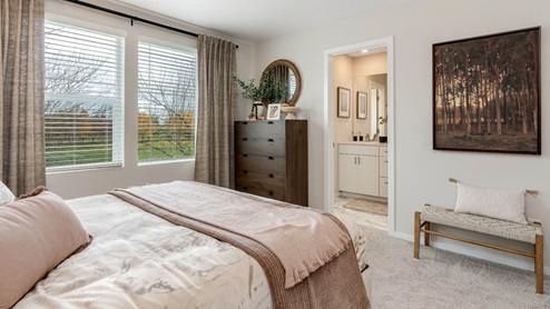 Lowrie Estates Primary bedroom with king bed and carpeting flooring with two accent tables and drapes on the windows