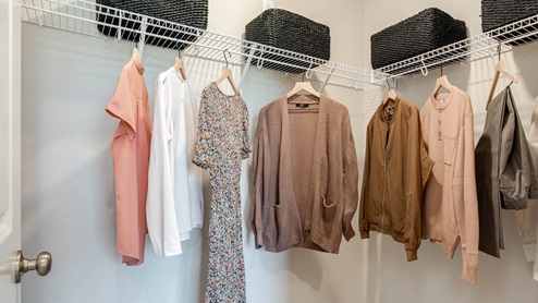Lowrie Estates walk in closet with white wire shelving and clothes hanging with storage boxes above