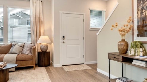 Scholls Meadow entry with laminate flooring, white staircase, entryway table with a plant and painting over top, side table, window next to door, gray rug, coffee table, and windows