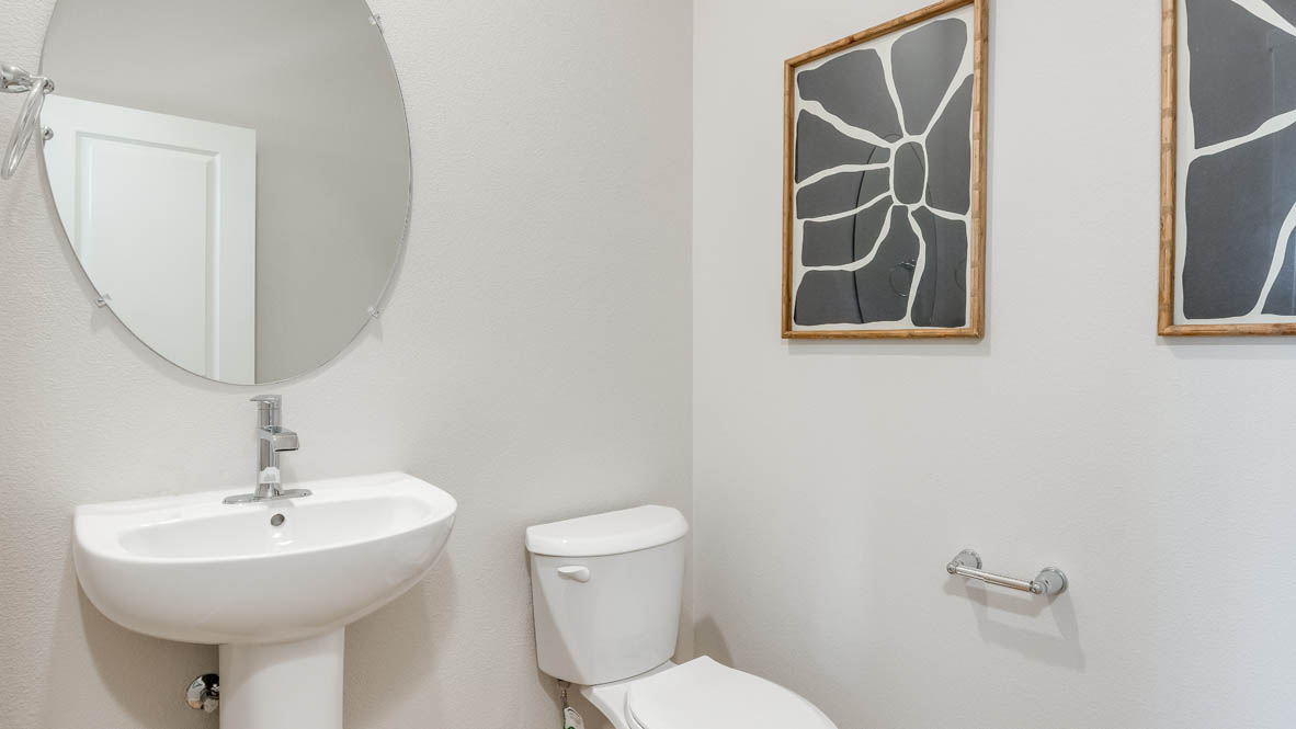 Davis Estates Powder Room with circular mirror, single sink vanity, toilet, and paintings