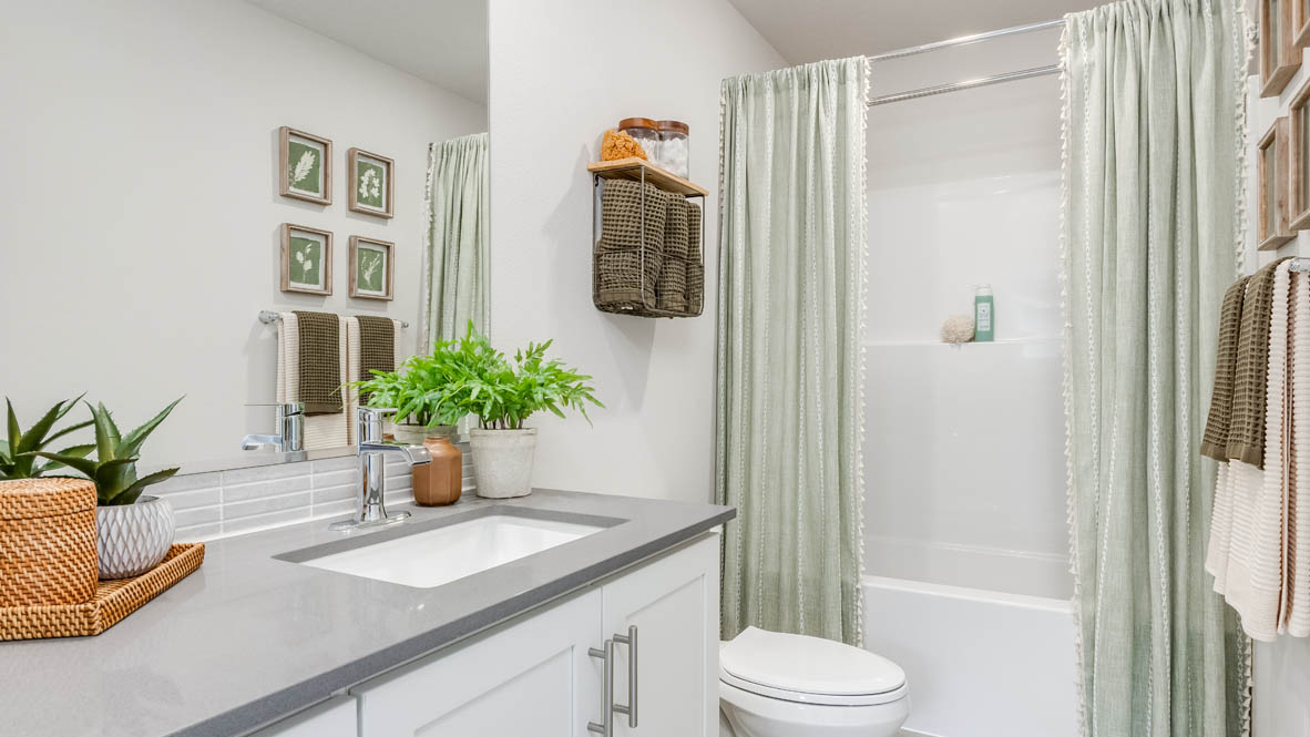 Davis Estates secondary bathroom with quartz countertops, mirror, sink with undermount bowl, cabinets, toilet, green shower curtain, and bathtub
