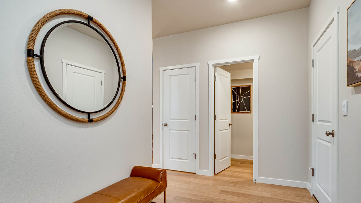 Davis Estates Entry with circular mirror and entry stool, laminate flooring, white walls, door to the powder room, and walkway to the great room and kitchen