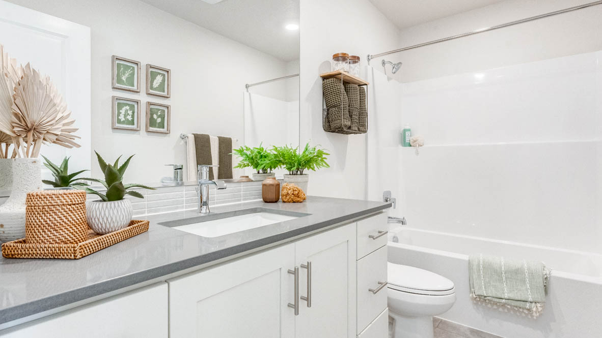 Davis Estates secondary bathroom with quartz countertops, mirror, sink with undermount bowl, cabinets, toilet, green shower curtain, and bathtub