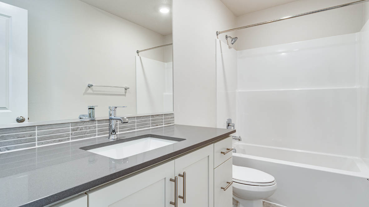 Davis Estates secondary bathroom with gray countertops and shaker style cabinets with brushed nickel pulls and a tub shower