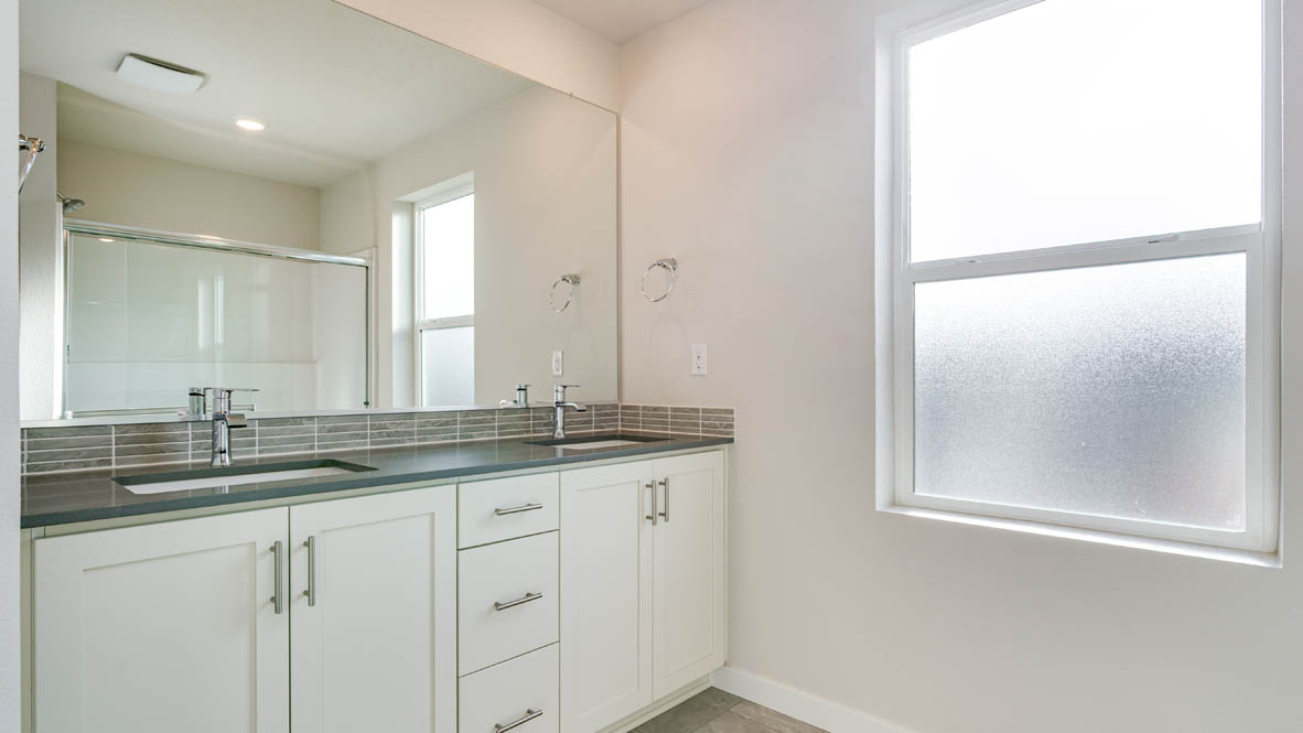 Davis Estates primary en suite bathroom with gray solid surface countertops and shaker style cabinets with brushed nickel pulls and a walk in shower