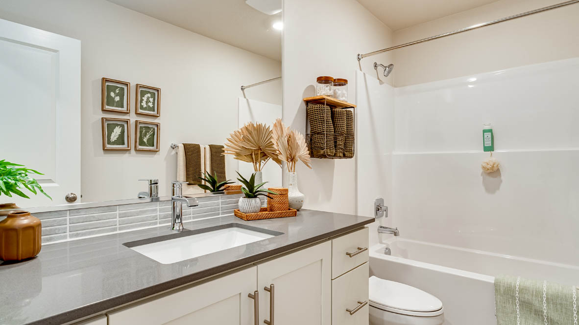 Davis Estates secondary bathroom with quartz countertops, mirror, sink with undermount bowl, cabinets, toilet, green shower curtain, and bathtub