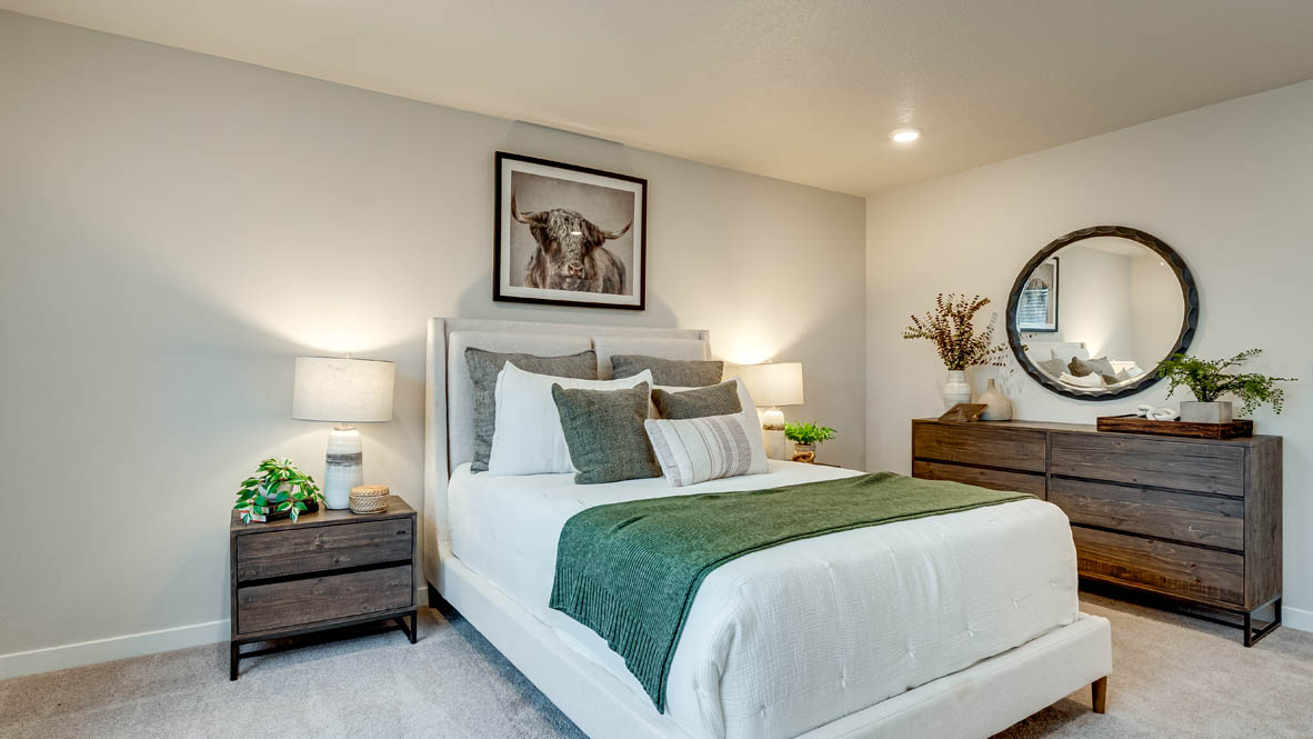 Davis Estates Primary bedroom with white comforter and green accent blanket, dresser with a plant, circle mirror, two paintings, and view of the primary bathroom
