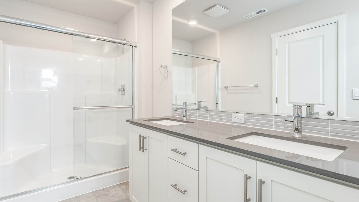 Davis estates primary bathroom with solid surface countertops, mirror, walk in shower, and cabinets