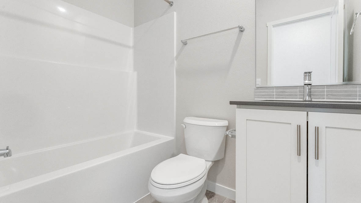 Davis Estates Downstairs bathroom with toilet, mirror, tub, and white cabinets