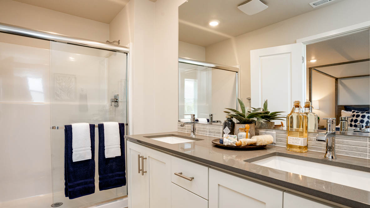 Davis estates primary bathroom with solid surface countertops, mirror, walk in shower, and cabinets