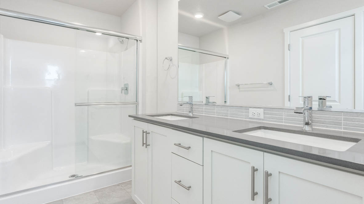 Davis estates primary bathroom with solid surface countertops, mirror, walk in shower, and cabinets