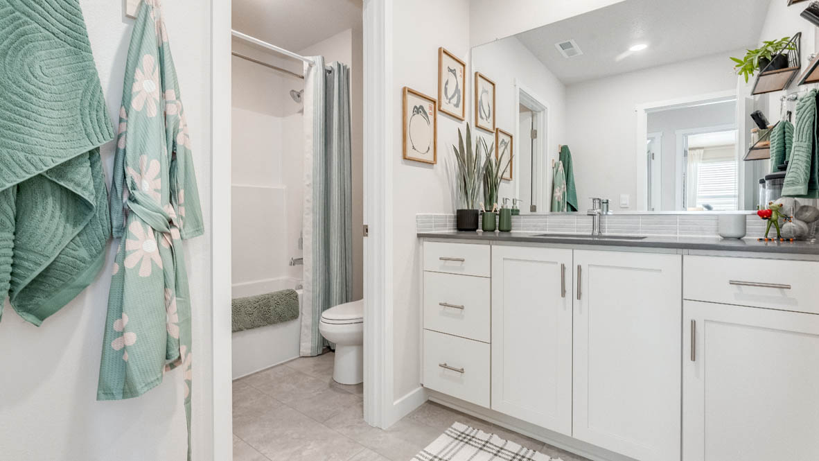 Davis Estates secondary bathroom with quartz countertops, double vanity, mirror, decorative towel set, privacy toilet, and shower tube