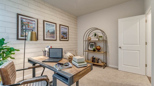 Marcola Meadows den with carpeting, shiplap accent wall, desk set up with a leather chair, three art prints, and a bookshelf