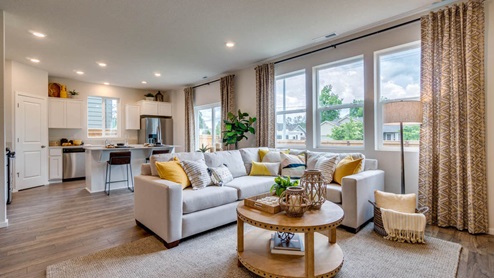 Marcola Meadows great room with a yellow accent wall with a fire place and a tv mounted above it, an l shaped sectional and coffee table over an area rug, with a brown chair and two brown wooden accent cabinets on either side of the tv