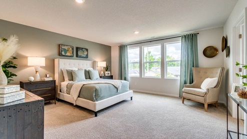 Marcola Meadows Primary Bedroom with carpeted flooring, grayish green accent wall, white fabric bedframe with light sage bedding, and brown wood accent furniture