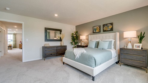 Marcola Meadows Primary Bedroom with carpeted flooring, grayish green accent wall, white fabric bedframe with light sage bedding, and brown wood accent furniture