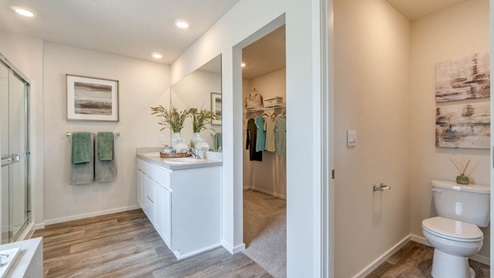 Marcola Meadows primary bathroom with two sink vanity, toilet closet, walk in shower with glass doors, laminate flooring and a carpeted walk in closet