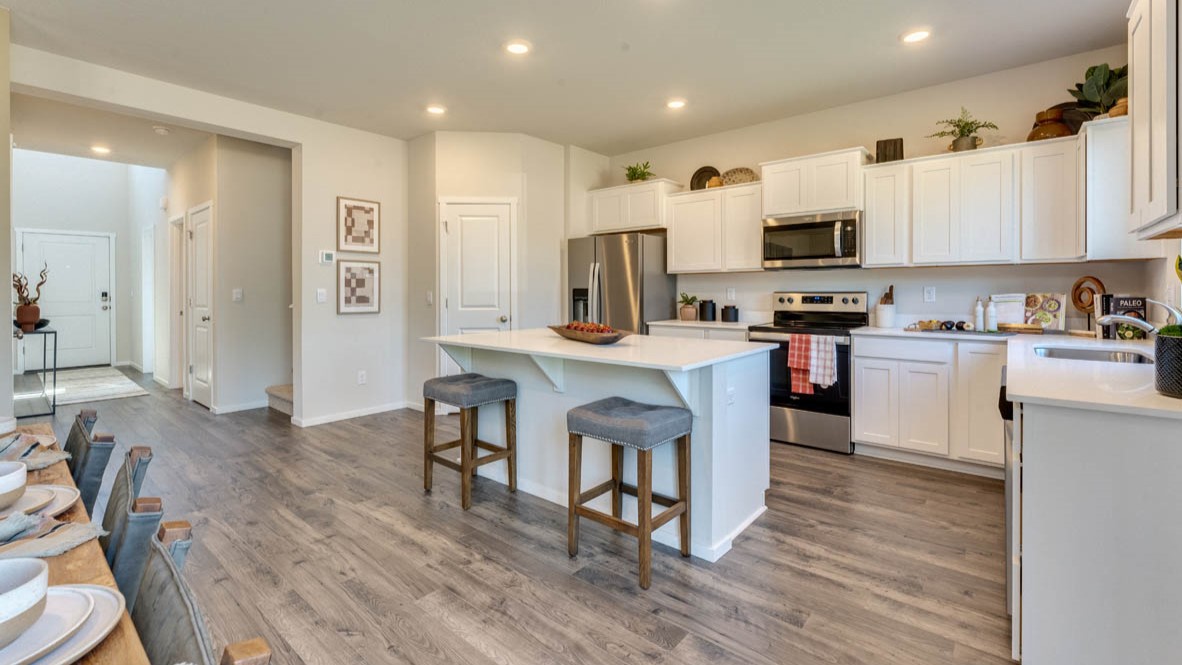 Eden Estates Kitchen with solid quartz countertops, in-island sink with a breakfast bar, stainless steel appliances, shaker style cabinets, pantry, decorative hanging decoration, dining room table, sliding glass door with shades