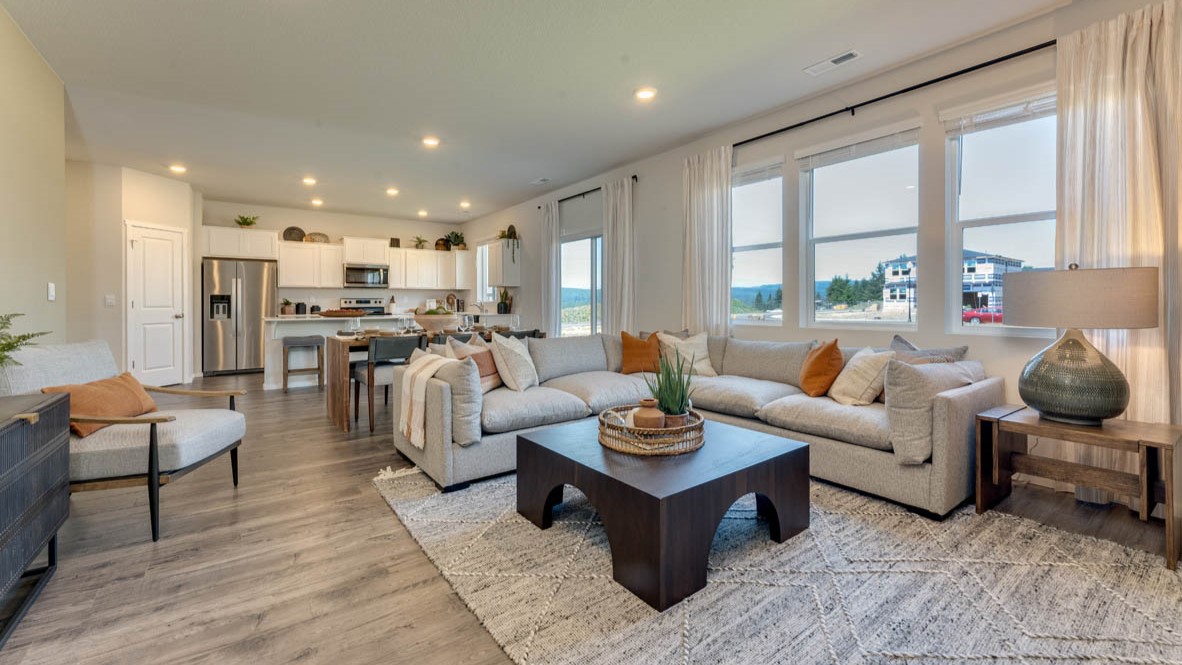 Eden Estates great room with couch, chair, coffee table, rug, and the kitchen and dining room in the background