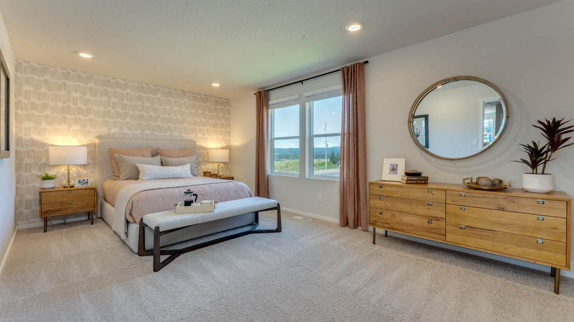 Eden Estates Primary bedroom with white carpet, three hanging paintings, two side tables, two lamps, a chair, windows with curtains