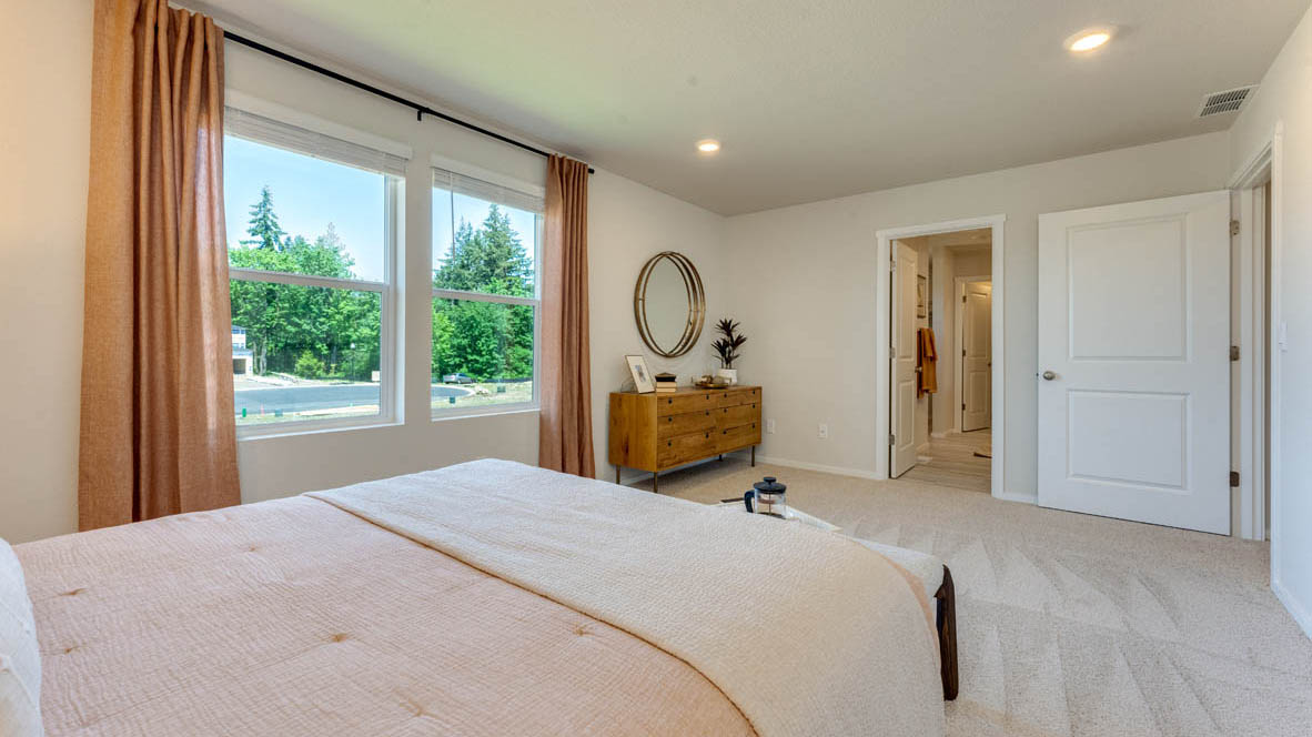 Eden Estates Primary bedroom with white carpet, three hanging paintings, two side tables, two lamps, a chair, windows with curtains