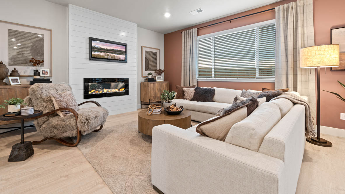 Sorrento Estates great room with L shaped sectional couch, carpeting, and center coffee table as well as window drapes, fireplace on a shiplap wall, and a fuzzy corner chair