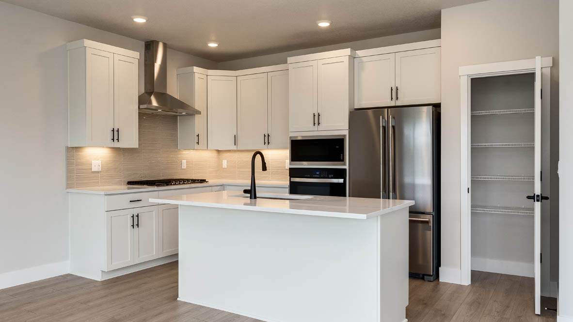 Sorrento Estates kitchen with white solid surface countertops and white shaker style cabinets and full height tile backsplash with hood vent and stainless steel appliances