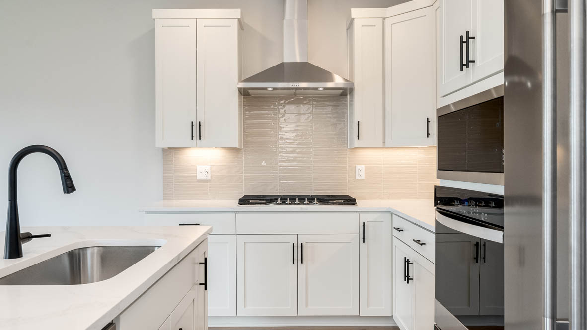 Sorrento Estates kitchen with white solid surface countertops and white shaker style cabinets and full height tile backsplash with hood vent and stainless steel appliances