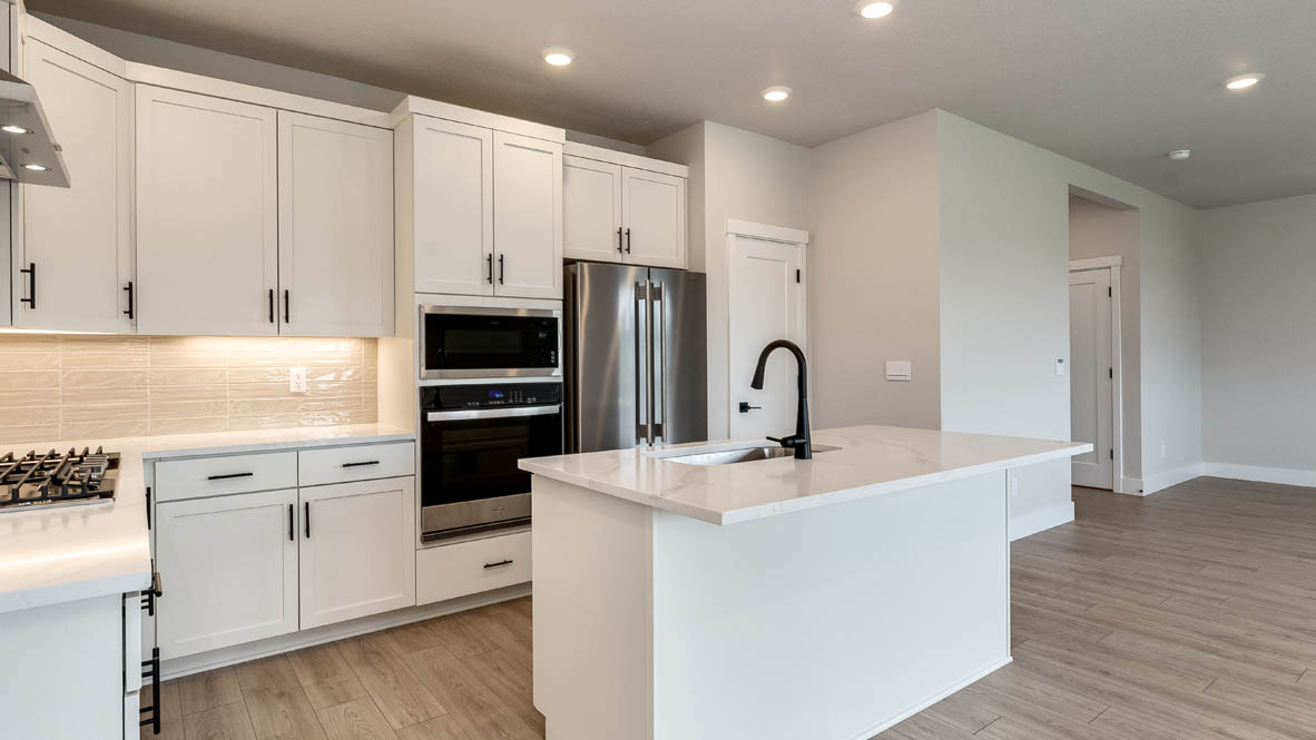 Sorrento Estates kitchen with white solid surface countertops and white shaker style cabinets and full height tile backsplash with hood vent and stainless steel appliances