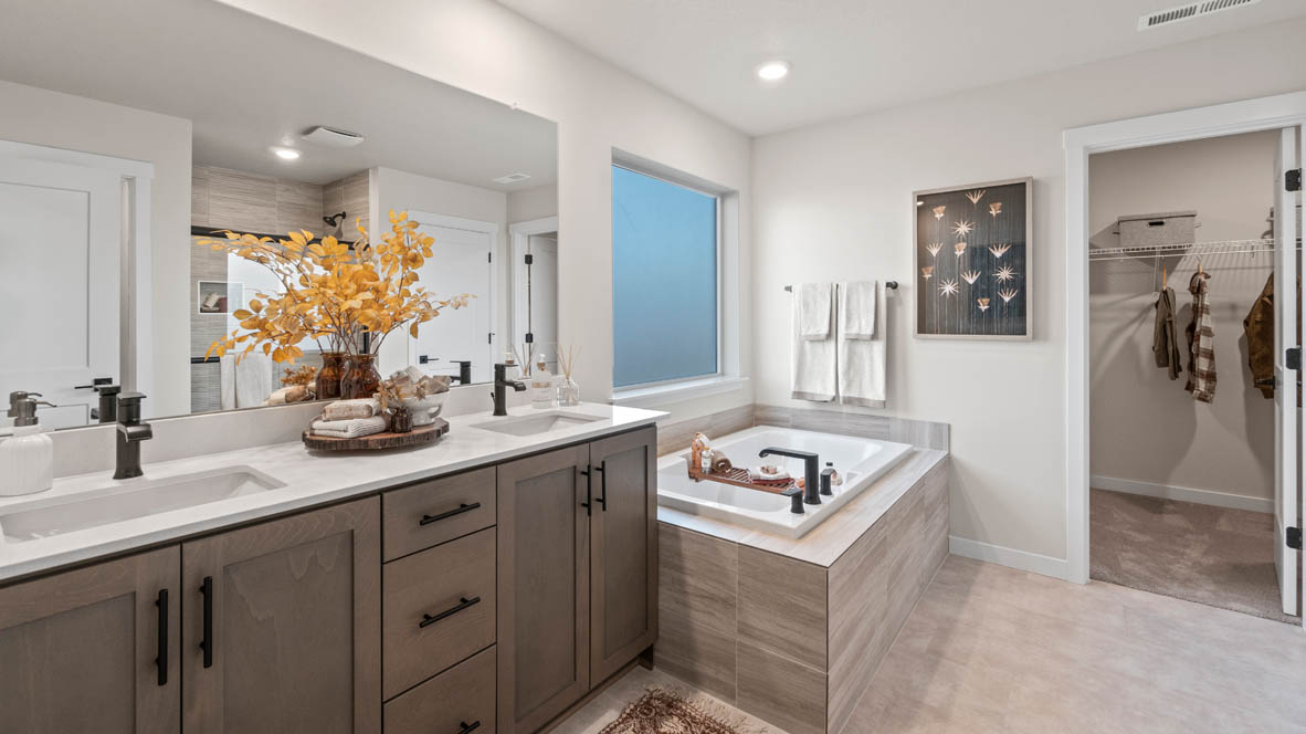 Sorrento Estates Primary bathroom with dark stained cabinetry, two sink vanity, bathtub, walk in closet, and shower