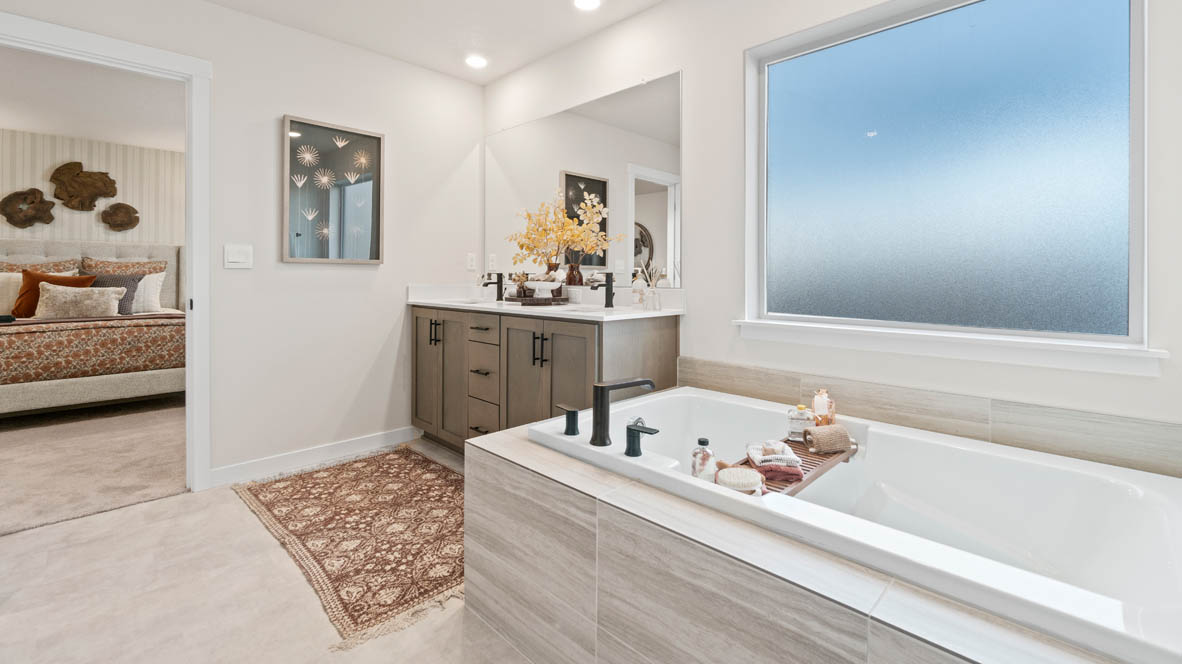 Sorrento Estates Primary bathroom with dark stained cabinetry, two sink vanity, bathtub, walk in closet, and shower