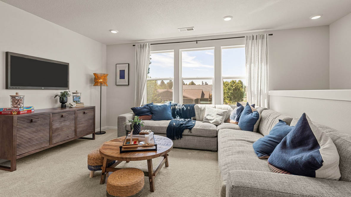 Monrovia carpeted Loft space with L shaped sectional couch, circular wooden coffee table with two small stools, a TV with a medial console underneath and three windows with drapes
