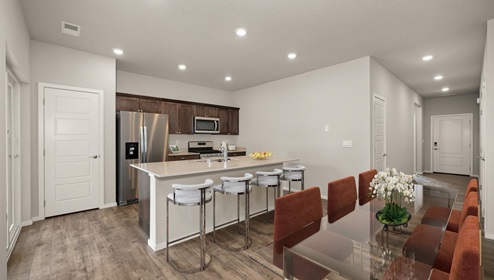 Dining area with a glass table and six burnt orange dining chairs, to the back left you can see the living area and the back right you can see into the kitchen area.
