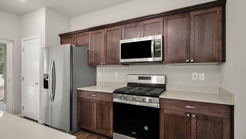 A kitchen with brown wood cabinets and stainless steel appliances, there's a large island in the middle with a quartz countertop and four white stools.