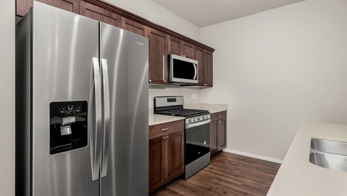 A kitchen with brown wood cabinets and stainless steel appliances, there's a large island in the middle with a quartz countertop and four white stools.
