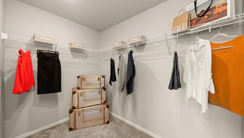A walk in closet with clothes hanging from wire shelving.