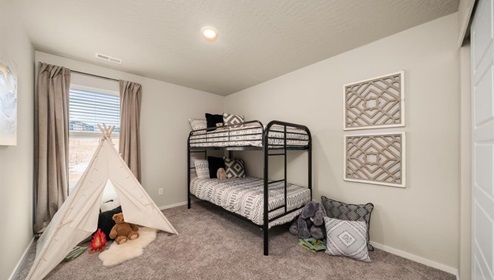 A bedroom with a metal framed bunk bed and two abstract art pieces on the right wall. There is a cloth teepee on the floor to the left in front of a window letting in natural light framed by beige curtains.
