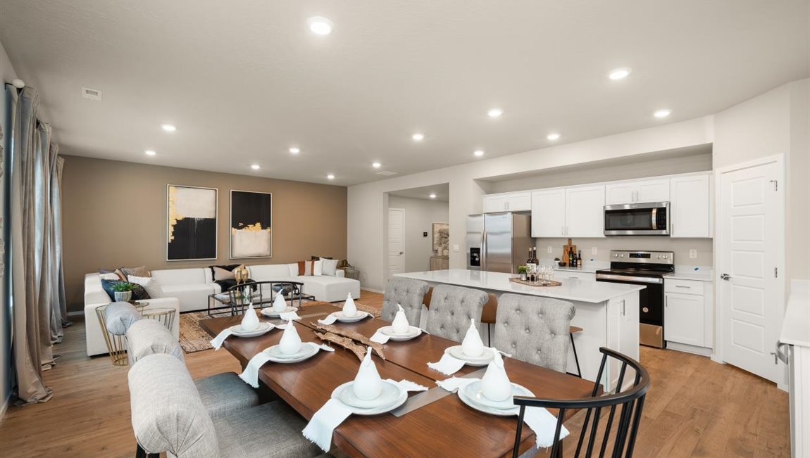 A kitchen with quartz countertops and white cabinets, a refridgerator to the left, and three burnt orange stools in front of the kitchen island. There's a window on the far wall letting in natural light.