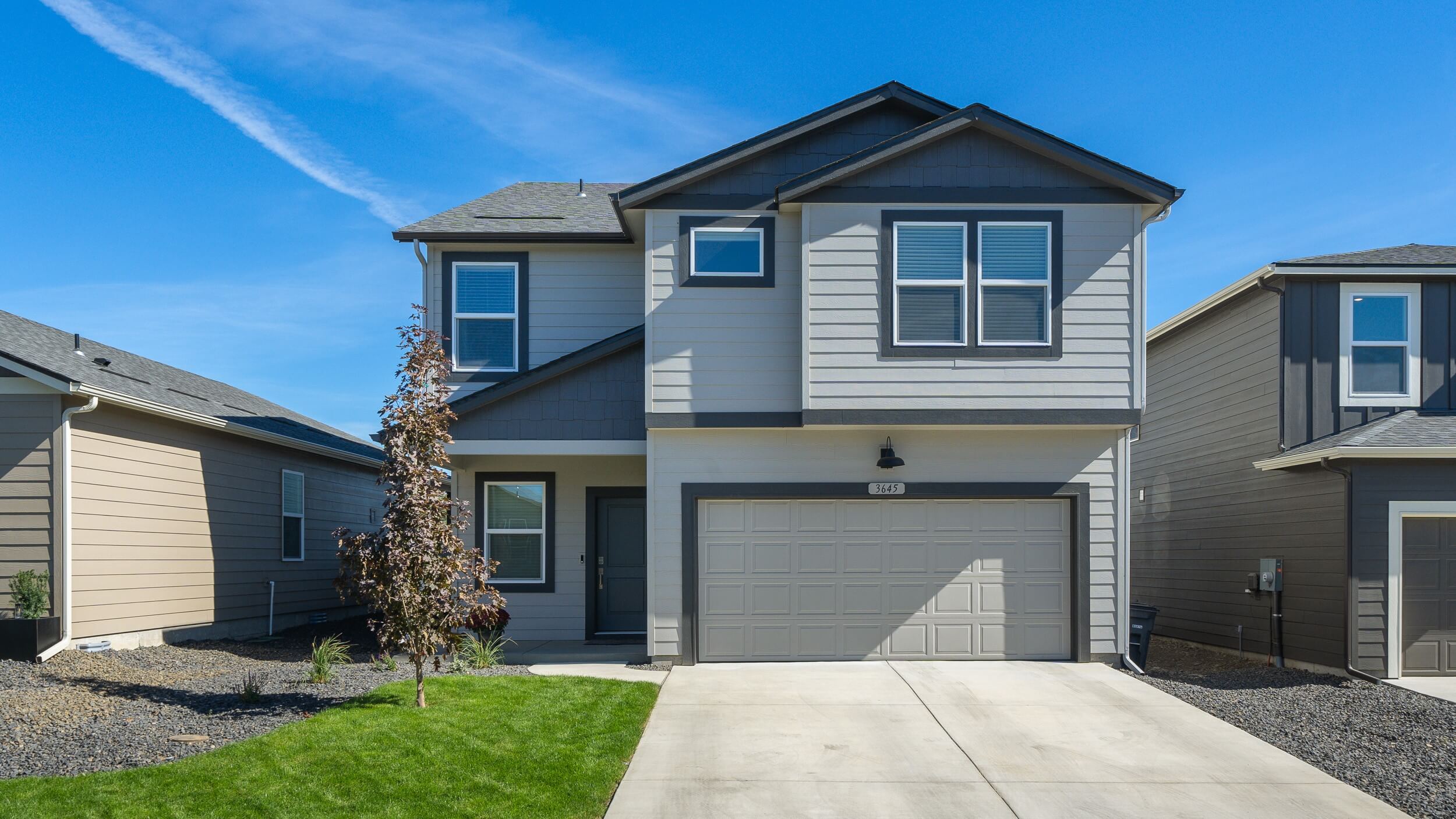 Photo of a two story home with off white and dark grey siding and dark accents and a dark roof.